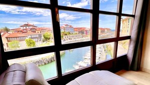 A room with a large window offering a view of a harbor and buildings.