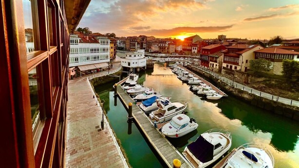 A marina with boats docked, a canal, and buildings in the background during sunset.