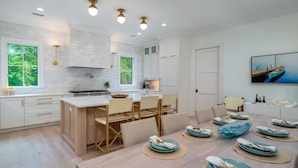 A modern kitchen with white cabinets, a central island, and a dining area with a table set for four. - Fabulous 5 BR/5.5 BA Home! New Construction! Pool! Screen Porch! Amenity access included (Seabrook Island)