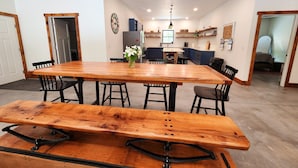 A spacious dining area with a large wooden table and benches, a kitchen in the background, and a visible door leading to another room. - Barndominium on H-58 near Pictured Rocks Attractions 
 (Shingleton)