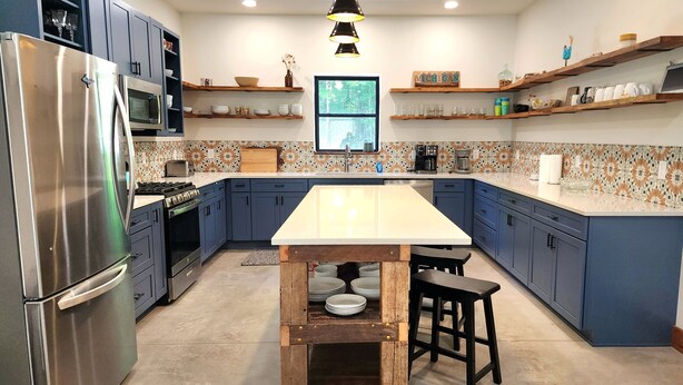A modern kitchen with a central island, stainless steel appliances, blue cabinets, and decorative tiles. - Barndominium on H-58 near Pictured Rocks Attractions 
 (Shingleton)