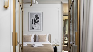 Moderni hotellihuone, jossa on suuri sänky, yöpöytä lampun kanssa ja seinällä kehystetty abstrakti taideteos.