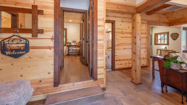 Un intérieur en bois avec une porte en bois, une pancarte de bienvenue, un banc et une table agrémentée d’une plante.