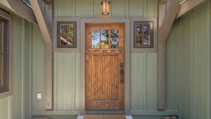 Une porte d’entrée en bois avec un panneau de verre, un paillasson et un luminaire placé au-dessus.