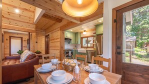 L’intérieur d’un chalet en bois comprend un coin repas préparé pour un repas, un salon avec un canapé et une cuisine dotée de meubles verts et d’appareils électroménagers modernes.