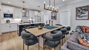 A modern kitchen with white cabinets, a central island, and a dining area with grey chairs. - Resonant - 2 Townhomes - 2 Private Rooftop Decks (Nashville)