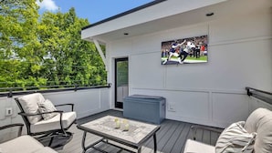 A deck with outdoor seating, a TV mounted on the wall, and a large air conditioning unit. - Resonant - 2 Townhomes - 2 Private Rooftop Decks (Nashville)