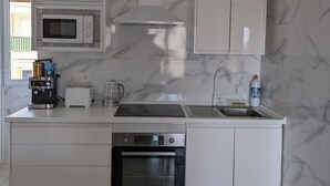 A modern kitchen with white cabinetry, a built-in microwave, a coffee maker, a toaster, and an oven. - Apartamento Santiago de la Ribera (San Javier)