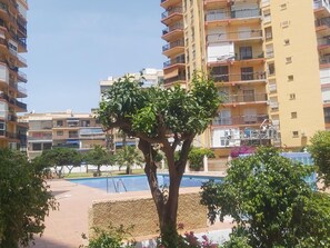 A residential building with multiple balconies, a swimming pool, and surrounding greenery.