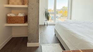 A bedroom with a large window, a bed, a wooden table, and built-in shelves with baskets. - Trendy & Cozy Downtown Halifax Condo (Halifax)