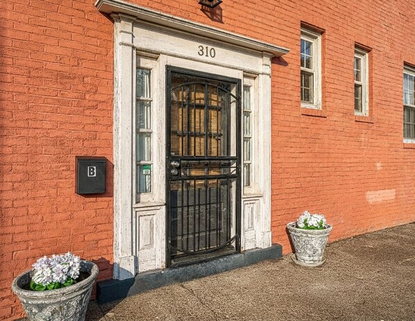 Un edificio de ladrillo rojo con una puerta negra, número 310, y dos macetas.