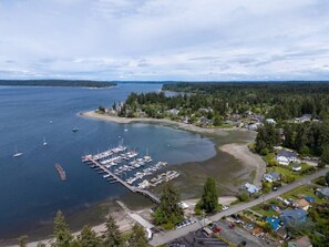 An aerial view of a coastal area with a marina, residential buildings, and a forested landscape.