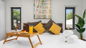Een moderne slaapkamer met een bed, kussens, een dienblad met een glas sinaasappelsap en opgerolde handdoeken.