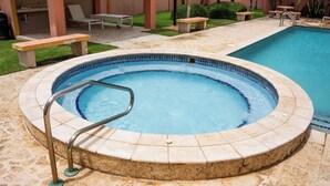 A hot tub with a tiled edge and a metal ladder, surrounded by a patio area with a pool.