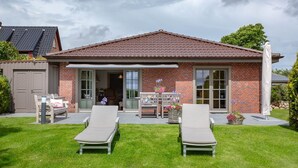 Une maison à deux étages avec une façade en briques, un toit en tuiles et un patio couvert comprenant deux fauteuils et une table.