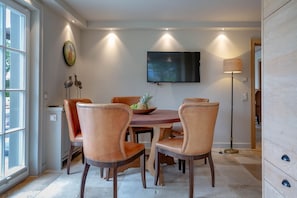 A dining area with a round table, six chairs, a television mounted on the wall, and a floor lamp.