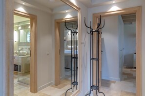 A hallway with a mirrored wall, a coat rack, and a glimpse of a bathroom with a sink and mirror.