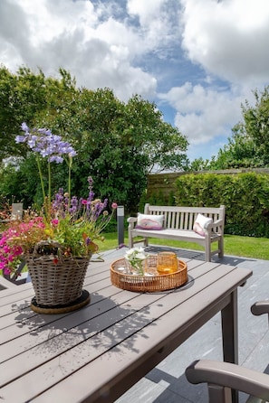 A wooden deck with a wicker basket filled with flowers and a wicker tray with a glass jar.