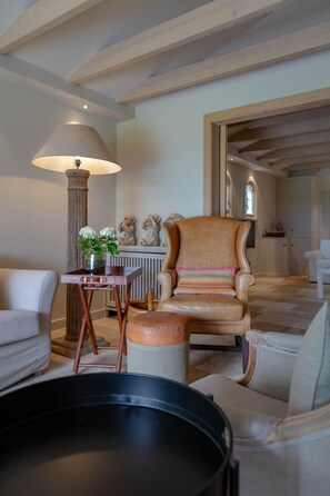 Amplio salón con techo alto, un sillón grande, una mesita de noche con una lámpara y vistas al área de la cocina.