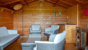 L’intérieur d’un chalet confortable, avec un mobilier en bois, une table à plateau de verre entourée de quatre chaises en osier, un plafond en bois et un buffet rustique en bois.