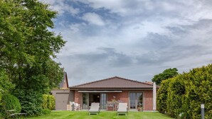 Une maison avec un toit recouvert de tuiles rouges, un patio abrité avec deux chaises et une pelouse bien entretenue.