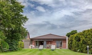 A house with a red-tiled roof, a covered patio with two chairs, and a well-maintained lawn.