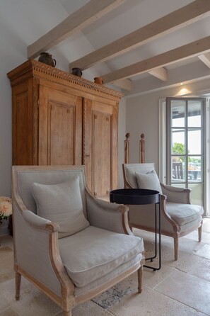 A room with two armchairs, a wooden cabinet, and a window with a view.
