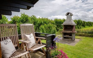 Un espacio de estar exterior de madera con dos sillas y una parrilla de piedra.