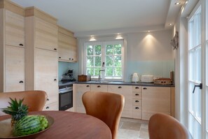 A modern kitchen with wooden cabinets, a large window, and a dining area with a table and chairs.