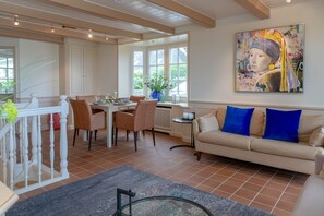 Un coin repas avec une table dressée pour quatre personnes, un canapé avec des coussins bleus et un grand tableau accroché au mur.