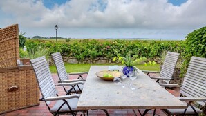 An outdoor patio with a table set for dining, surrounded by wicker chairs, and a view of a vineyard in the background. - Heefwai 2 - W1 - Holiday apartment "Heefwai 2 W1" in Morsum (Morsum)