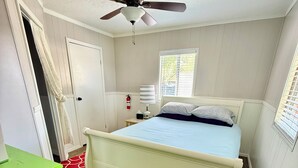 Una camera da letto con un letto, una ventola a soffitto, una finestra, una porta e un armadietto verde.