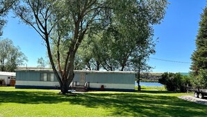 A mobile home with a small deck and a tree in front.