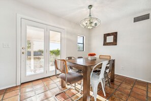 A dining area with a wooden table, six chairs, a chandelier, and a view through a sliding glass door to an outdoor patio. - LAZY H BAR RANCH ESTATE, 3 /2,  AC, Pool, Hot Tub, BBQ, Horses and Dogs Welcome! (Tucson)
