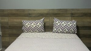 A bed with a striped bedspread and two patterned pillows against a wooden headboard. - Jbr park hotel (Goiania)