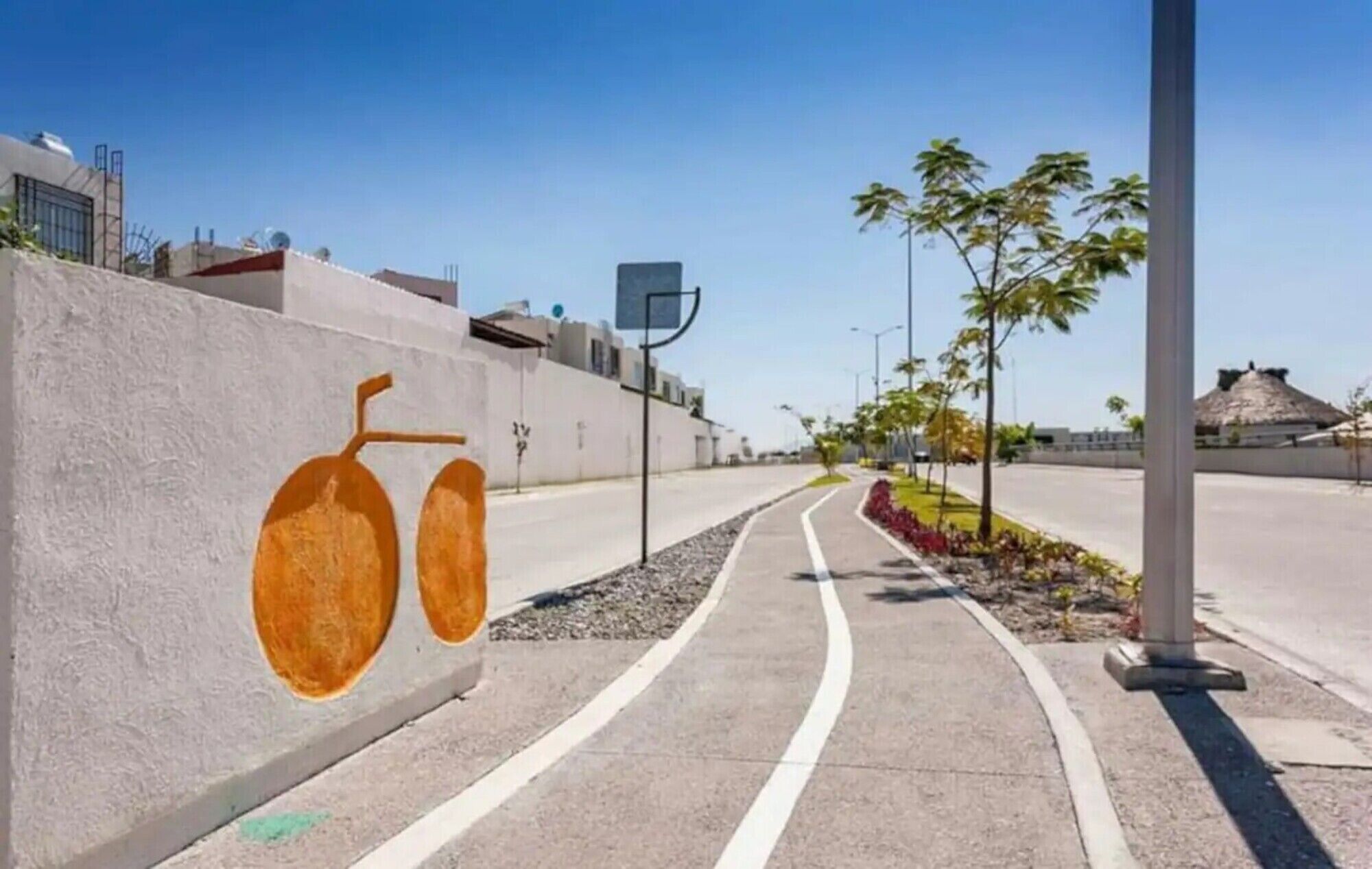 A paved pathway with a wall mural, palm trees, and a clear sky.