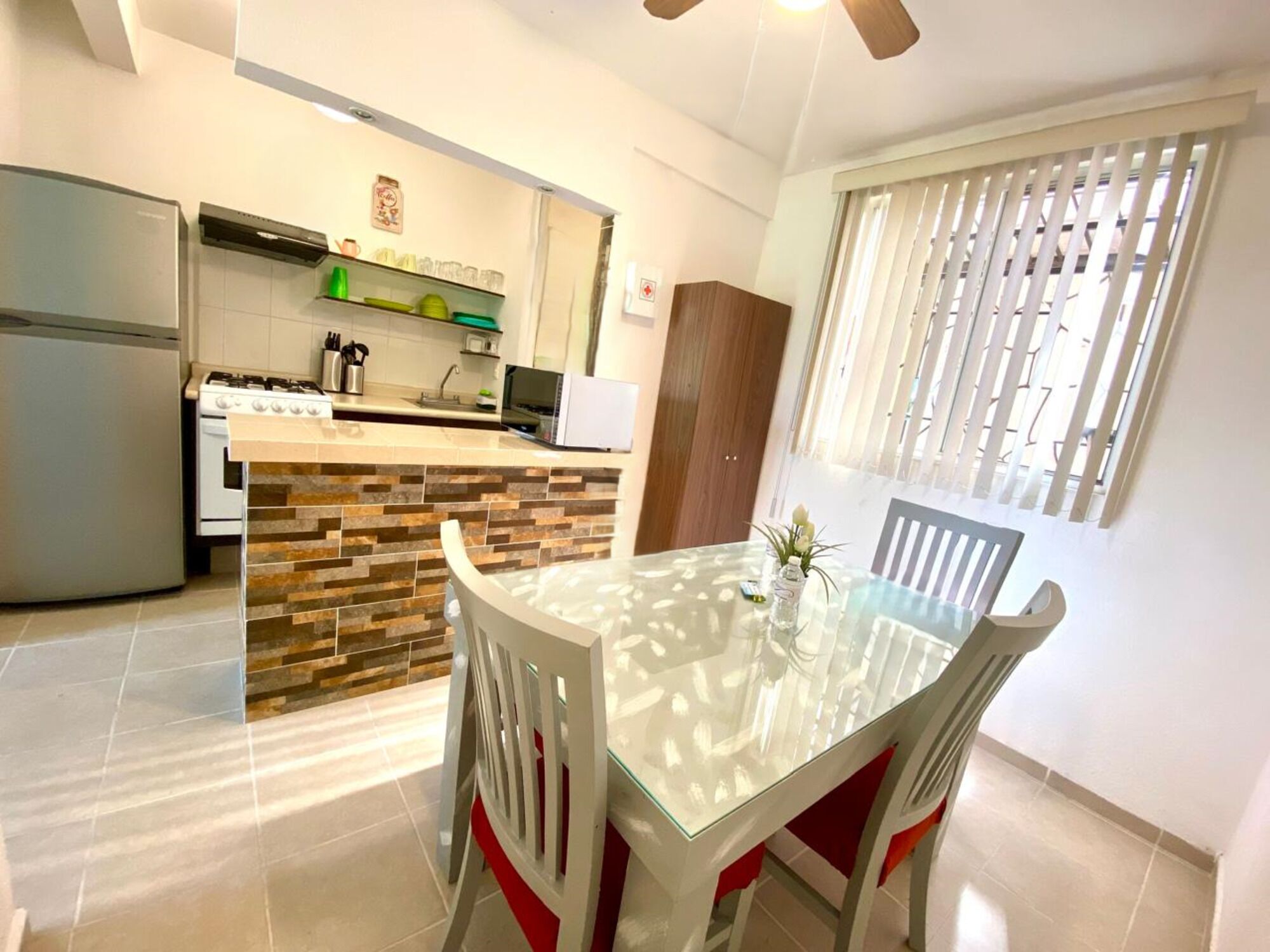 Une cuisine moderne dotée d’un îlot central intégré, d’une table à manger avec des chaises et d’une fenêtre avec des stores.