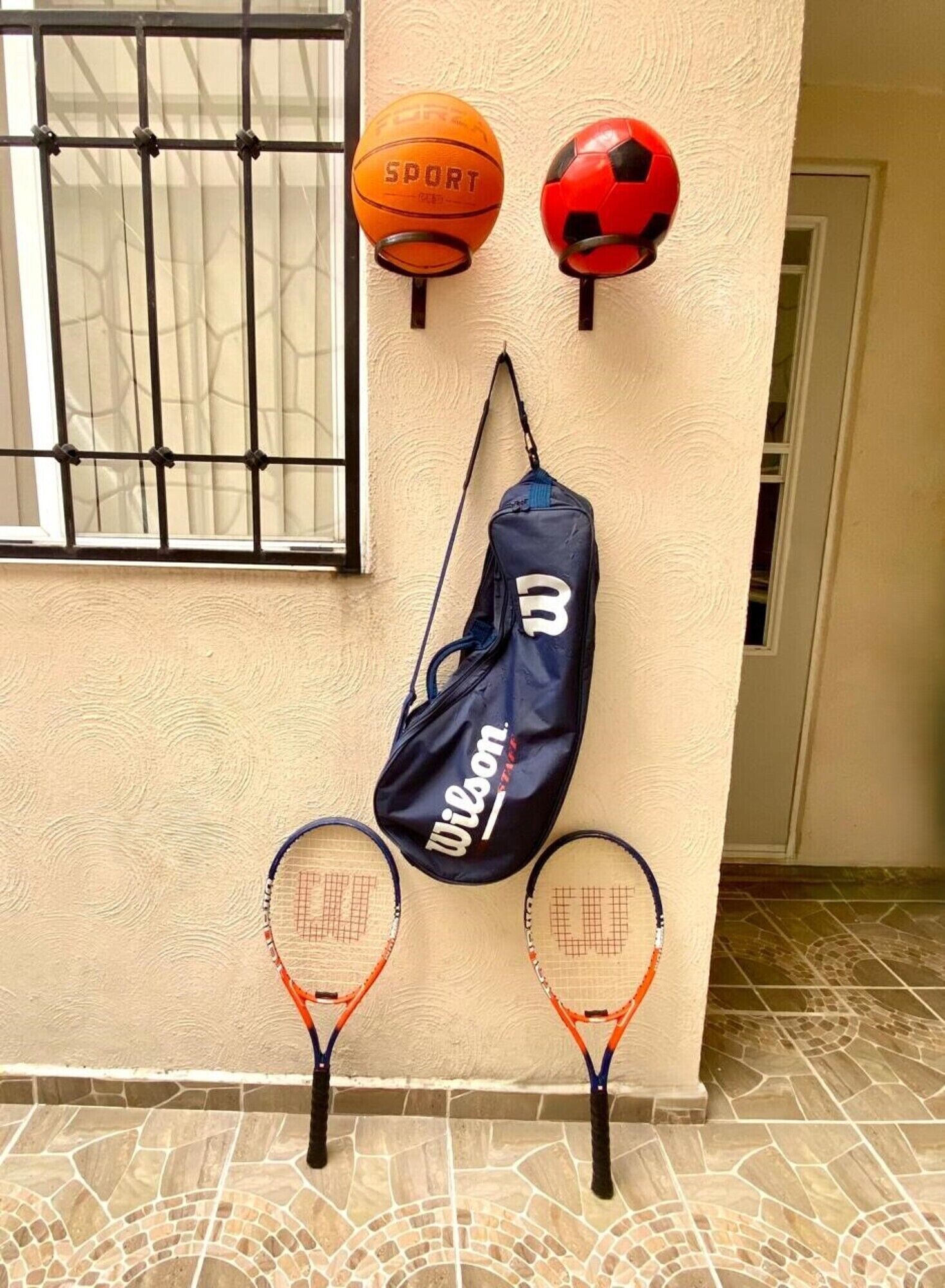 Une raquette de tennis appuyée contre un mur, un ballon de sport et un casque posés sur une porte.