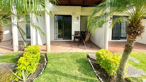 A covered patio area with a table and chairs, surrounded by potted plants and a well-maintained lawn.