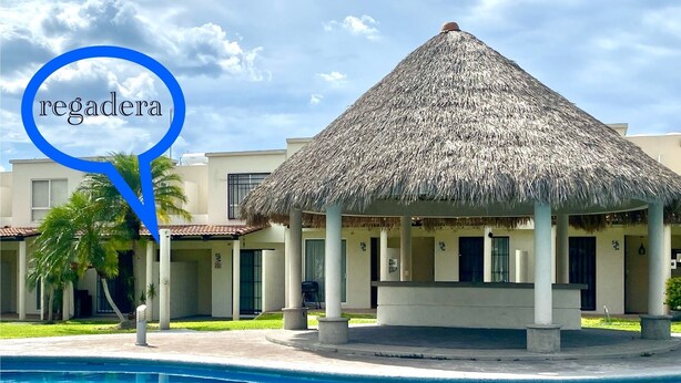 A pool area with a thatched-roof gazebo, palm trees, and a building with numbered doors.