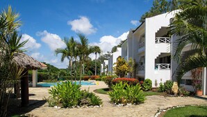 A resort with a swimming pool, palm trees, and a white building with balconies. - Costa del sol (Sosúa)