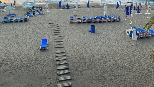 A beach with rows of sun loungers and umbrellas, a wooden walkway, and the ocean in the background. - Costa del sol (Sosúa)
