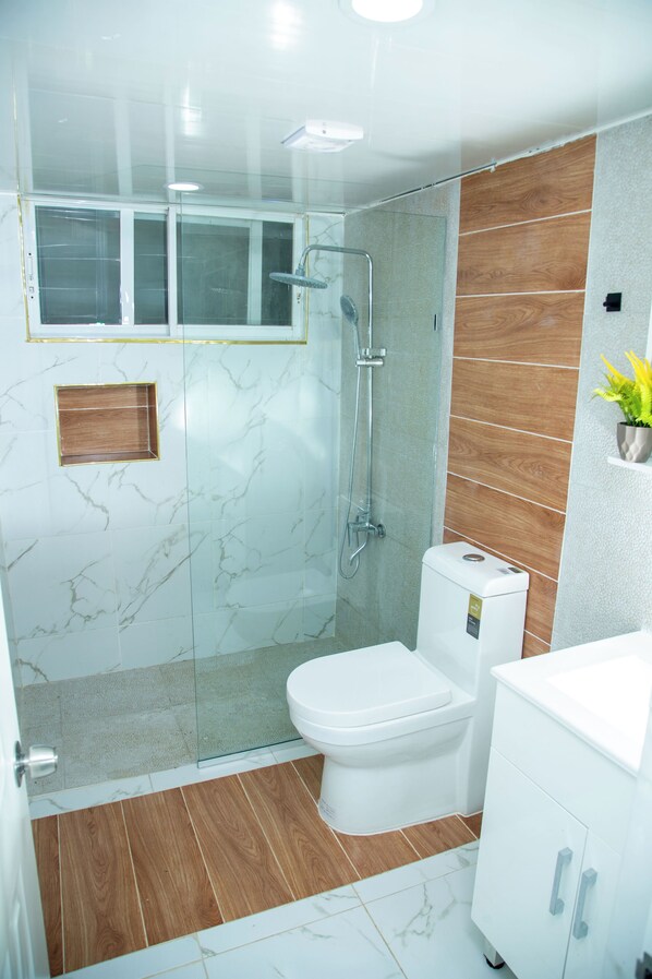 A modern bathroom with a glass-enclosed shower, a white toilet, and a wooden vanity.