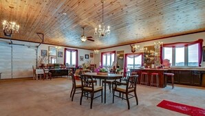 A spacious room with a wooden ceiling, a dining area with a round table and chairs, a kitchen with a bar, and large windows with curtains. - Charming castle with 7 bedrooms and WiFi, AC in Coe Hill (Coe Hill)