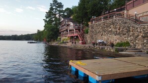 A lakeside property with a wooden dock, a stone retaining wall, and a building with a balcony overlooking the water. - Charming castle with 7 bedrooms and WiFi, AC in Coe Hill (Coe Hill)