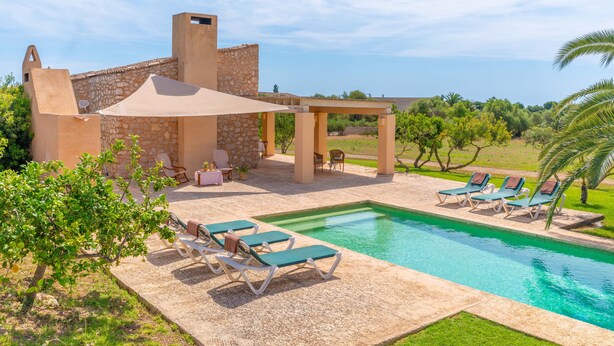 Zona de piscina con sillones de descanso, una pérgola y un edificio de piedra con vista al mar.