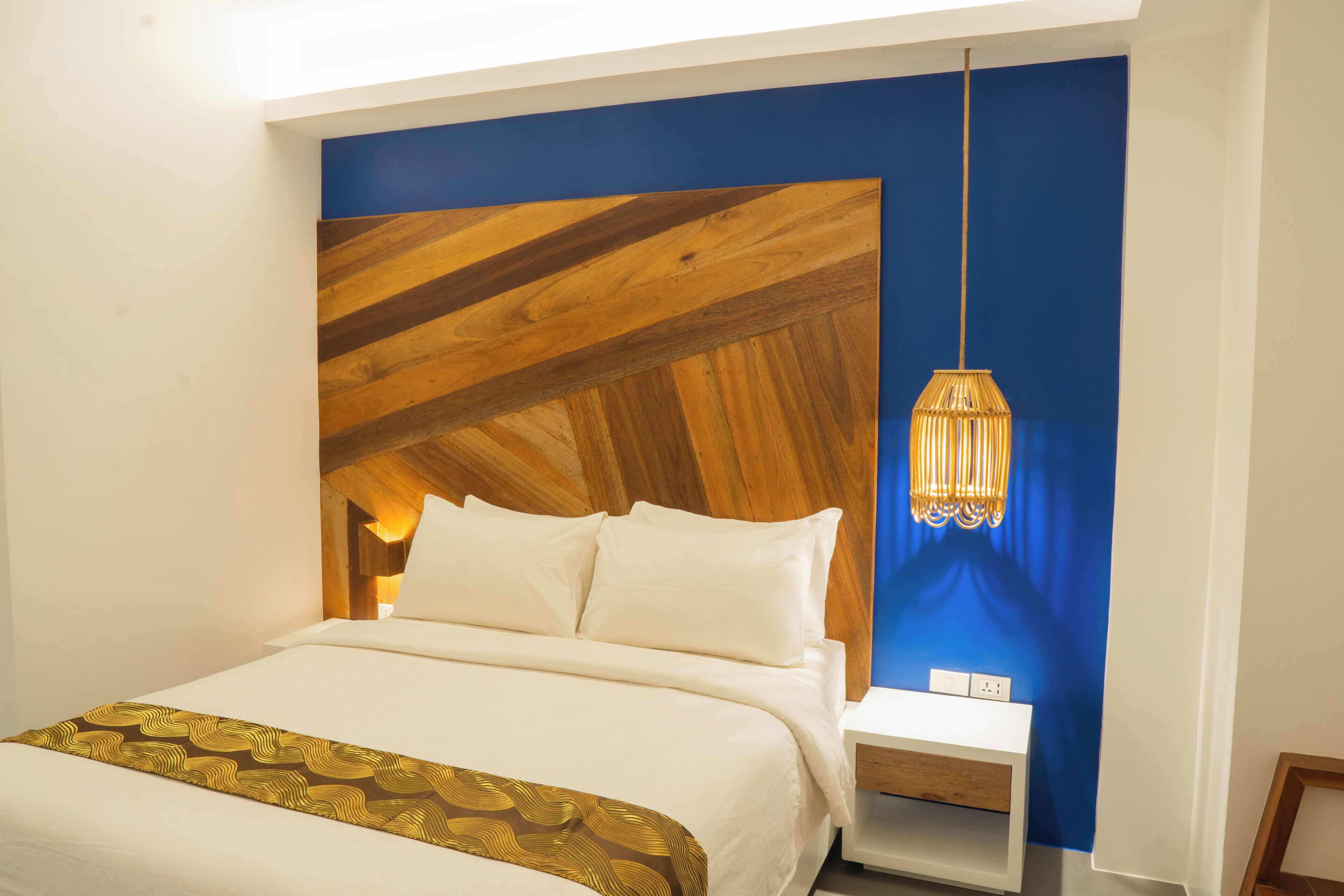 Ein modernes Schlafzimmer mit einem hölzernen Kopfteil, einem weißen Bett und einem Nachttisch mit Lampe.