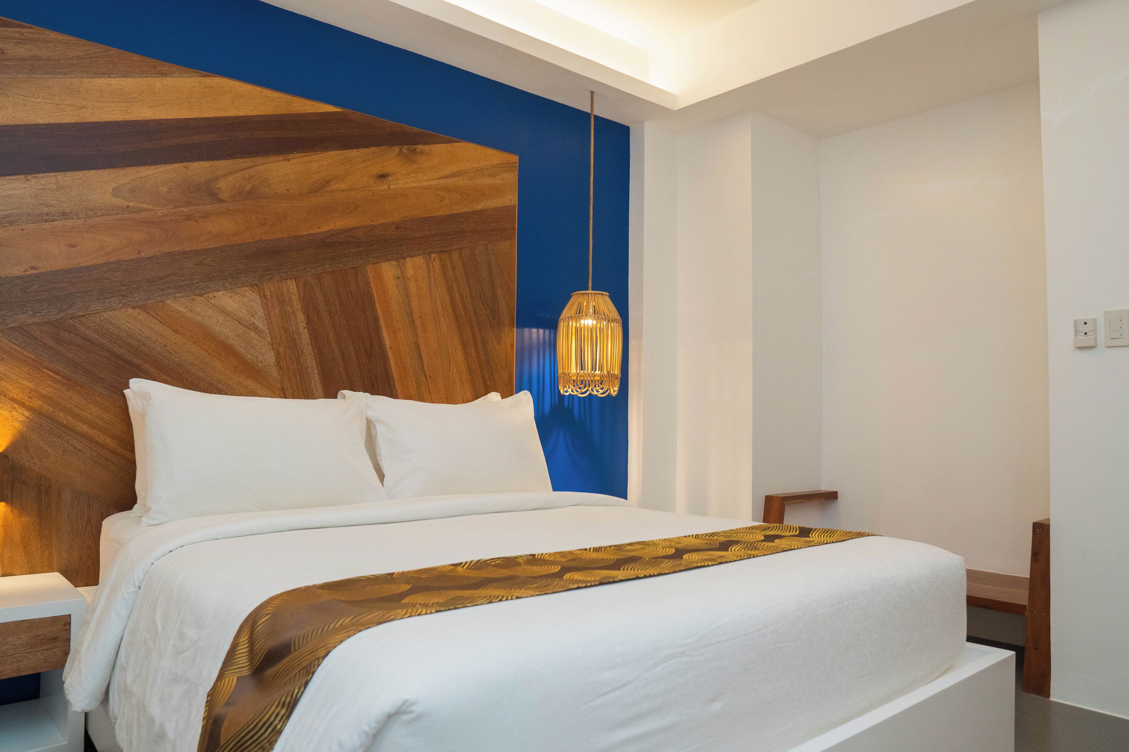 Une chambre d’hôtel moderne avec un grand lit, un mur décoratif en bois et une suspension lumineuse.