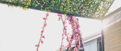 Una silla colgante con cojín, rodeada de un exuberante jardín vertical con flores rosadas.