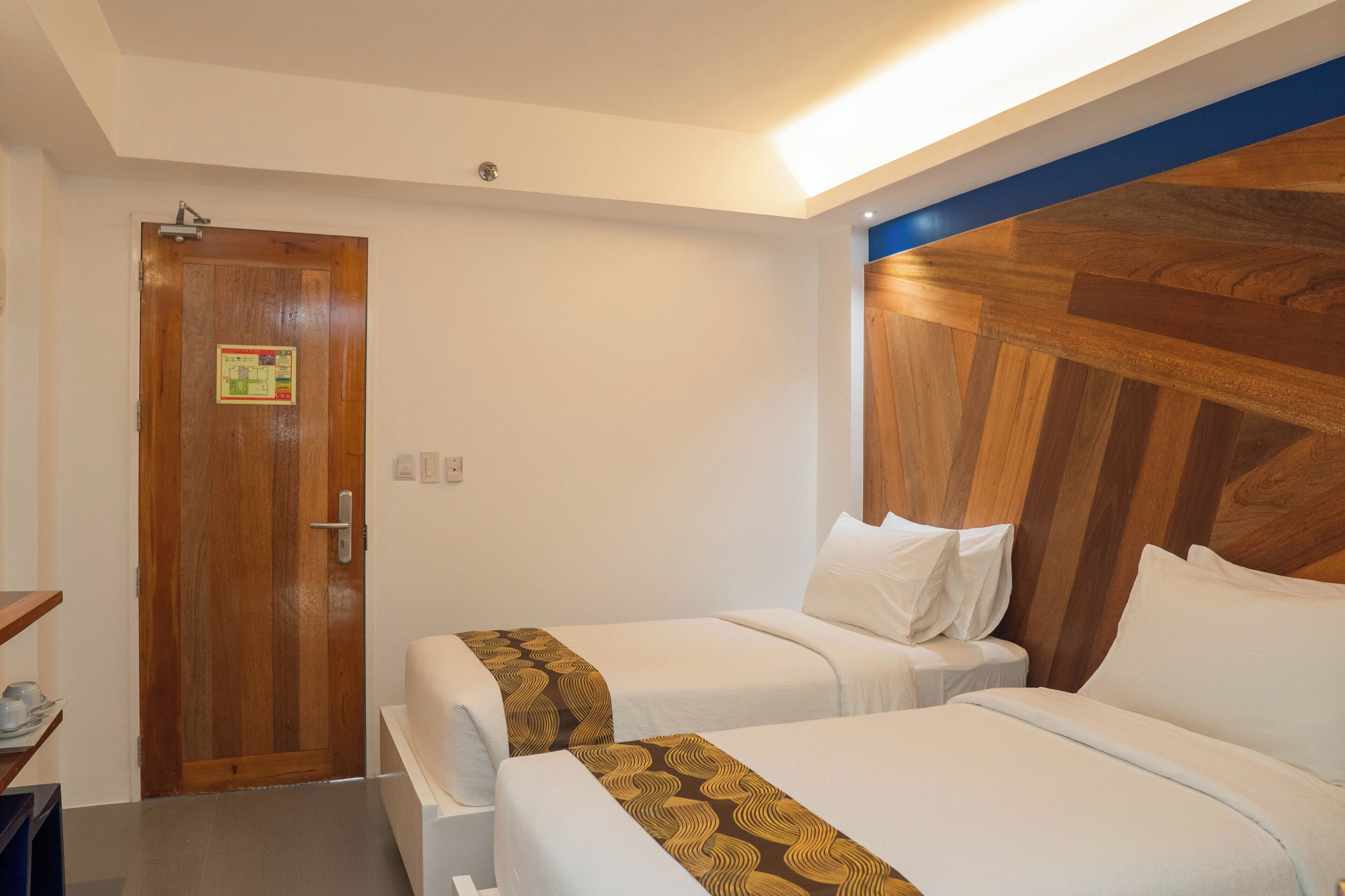 A hotel room with two beds, a wooden door, and a blue accent wall.